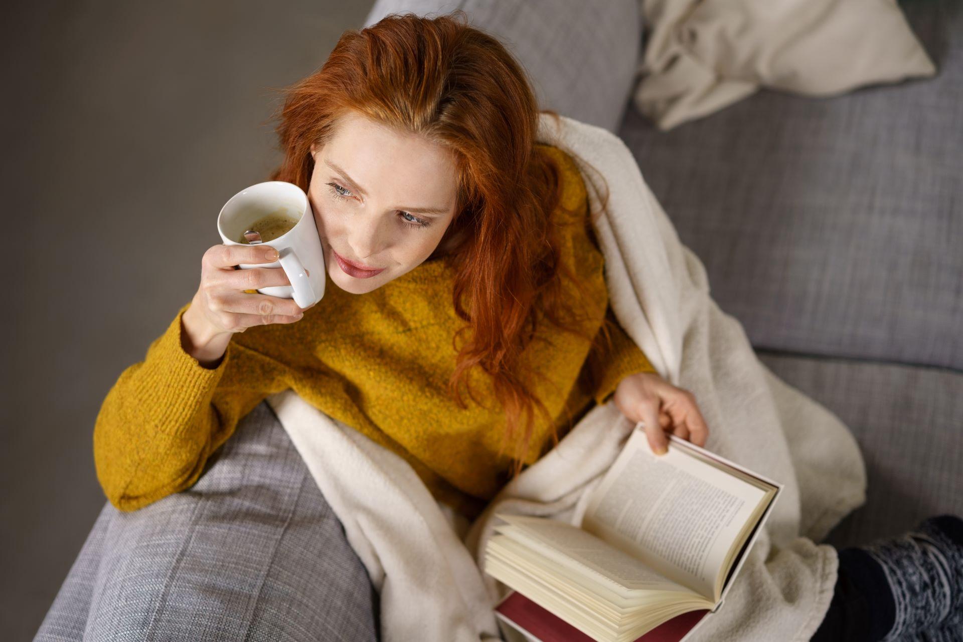 Frau mit einer Tasse Kaffee und einem Buch auf dem Sofa