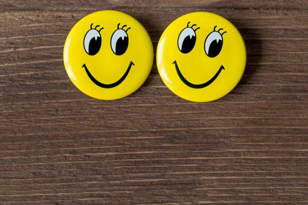 Zwei gelbe Smiley-Buttons auf Holzhintergrund – ideale Vorlage zum Buttons bestellen mit eigenem Motiv