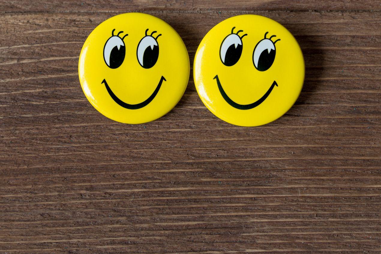 Zwei gelbe Smiley-Buttons auf Holzhintergrund – ideale Vorlage zum Buttons bestellen mit eigenem Motiv
